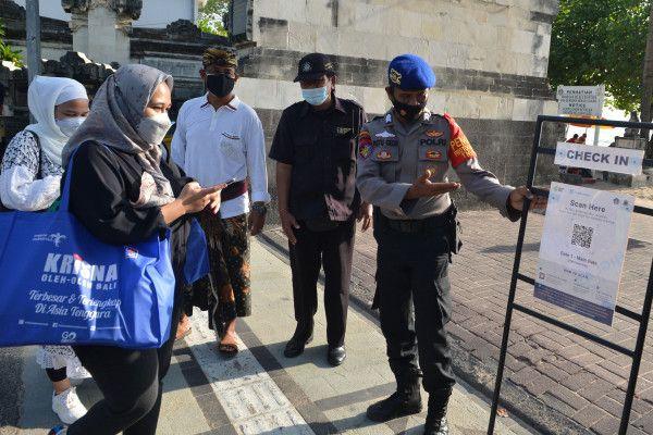 Petugas mengarahkan wisatawan untuk memindai QR Code dengan aplikasi PeduliLindungi sebelum memasuki kawasan wisata Pantai Kuta, Badung, Bali, Minggu (26/9/2021).