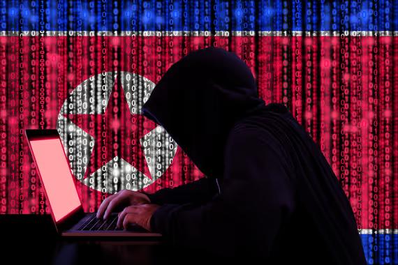 Hacker dalam hoody gelap duduk di depan notebook dengan Bendera Korea Utara. (Shutterstock/BeeBright)