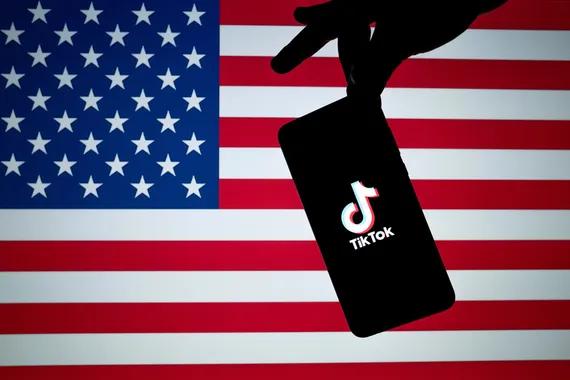 Logo TikTok terlihat pada siluet pegangan smartphone dengan bendera Amerika di bagian belakang. Shutterstock/Ascannio.